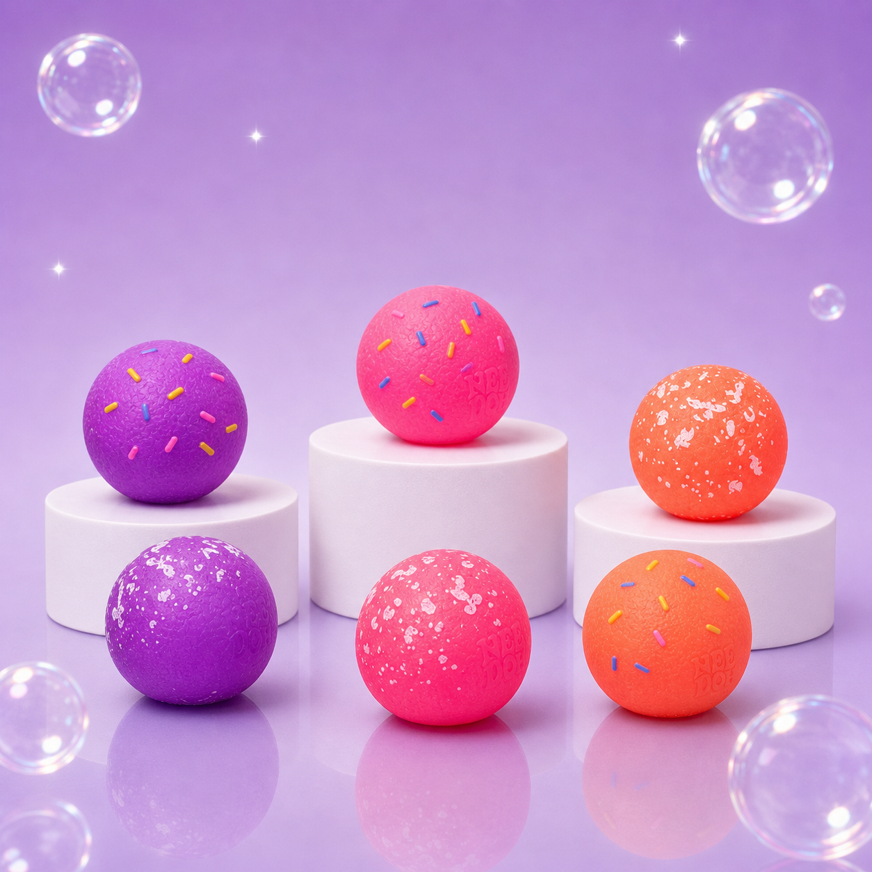 Six pink, purple, and orange NeeDoh Dohnut Holes with sprinkle and powdered finishes on white podiums.