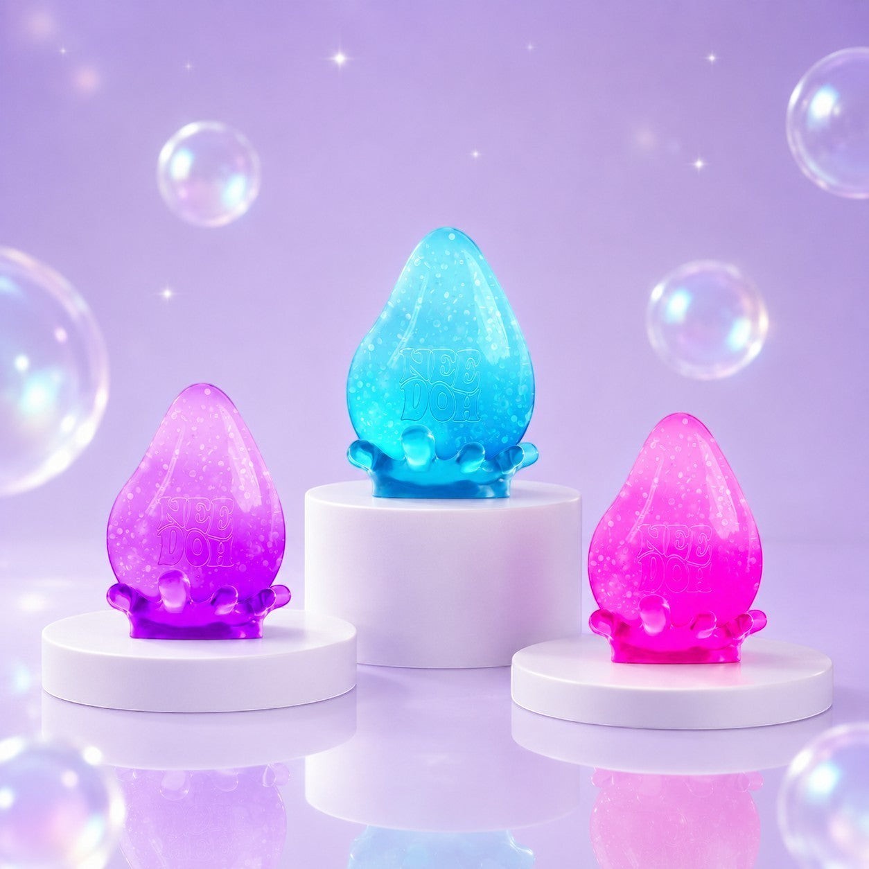 Squish Planet NeeDoh Dream Drop fidget toys in purple, blue, and pink on white pedestals with bubbles.