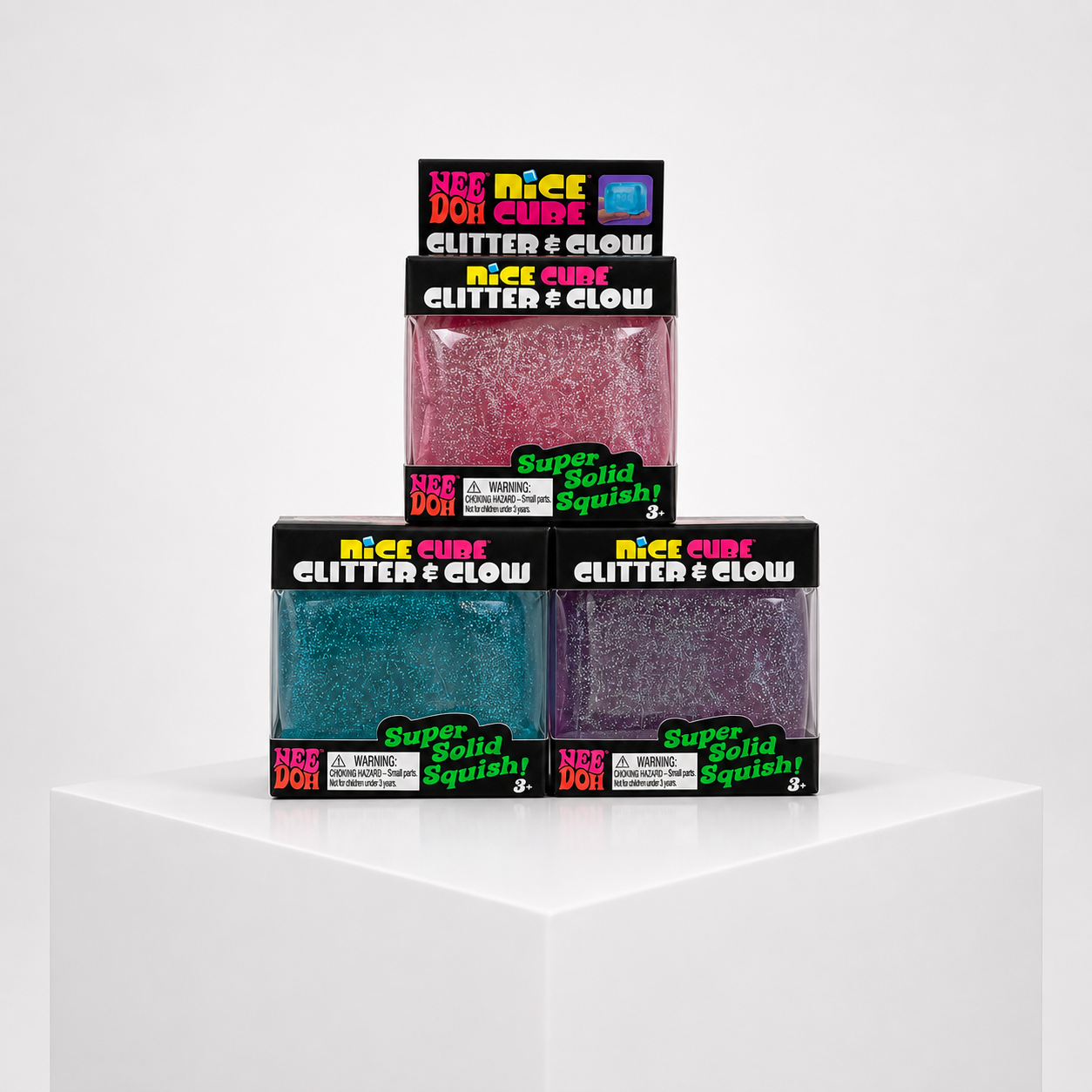 NeeDoh Nice Cube Glitter and Glow blue, pink, and purple variants in retail packaging, front group view.