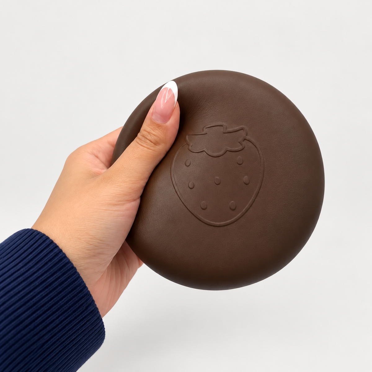 Hand squeezing the brown round Nunu toy with an embossed strawberry
