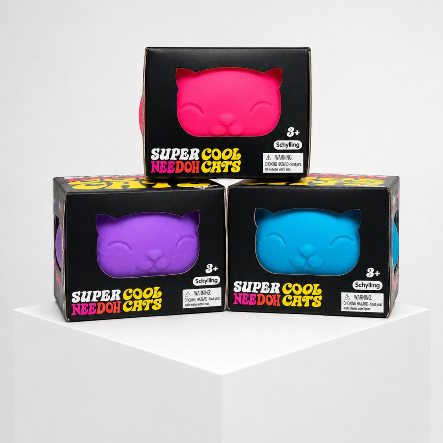 Squish Planet NeeDoh Super Cool Cat squishy fidget toys in pink, purple, and blue boxes stacked on a white pedestal.