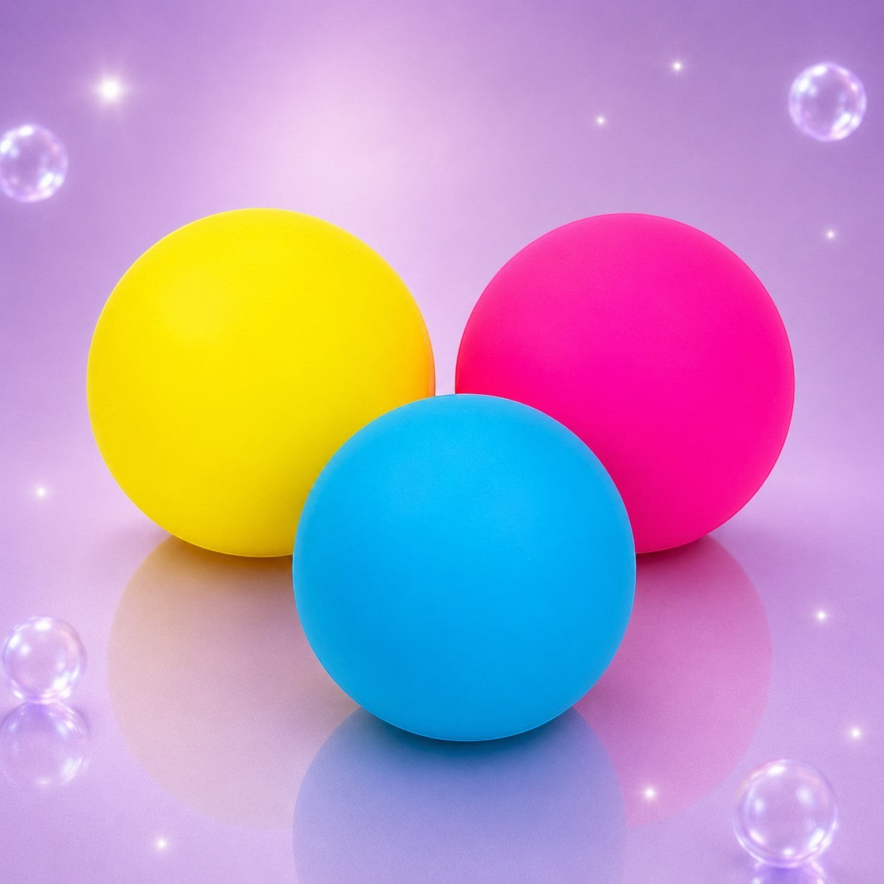 Squish Planet NeeDoh color changing squishy fidget balls in yellow, pink, and blue on a purple reflective surface.