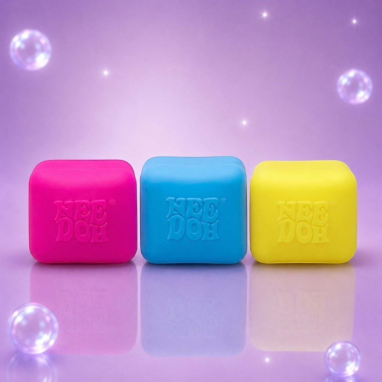 Squish Planet NeeDoh color changing cube fidget toys in pink, blue, and yellow on a purple background with bubbles.