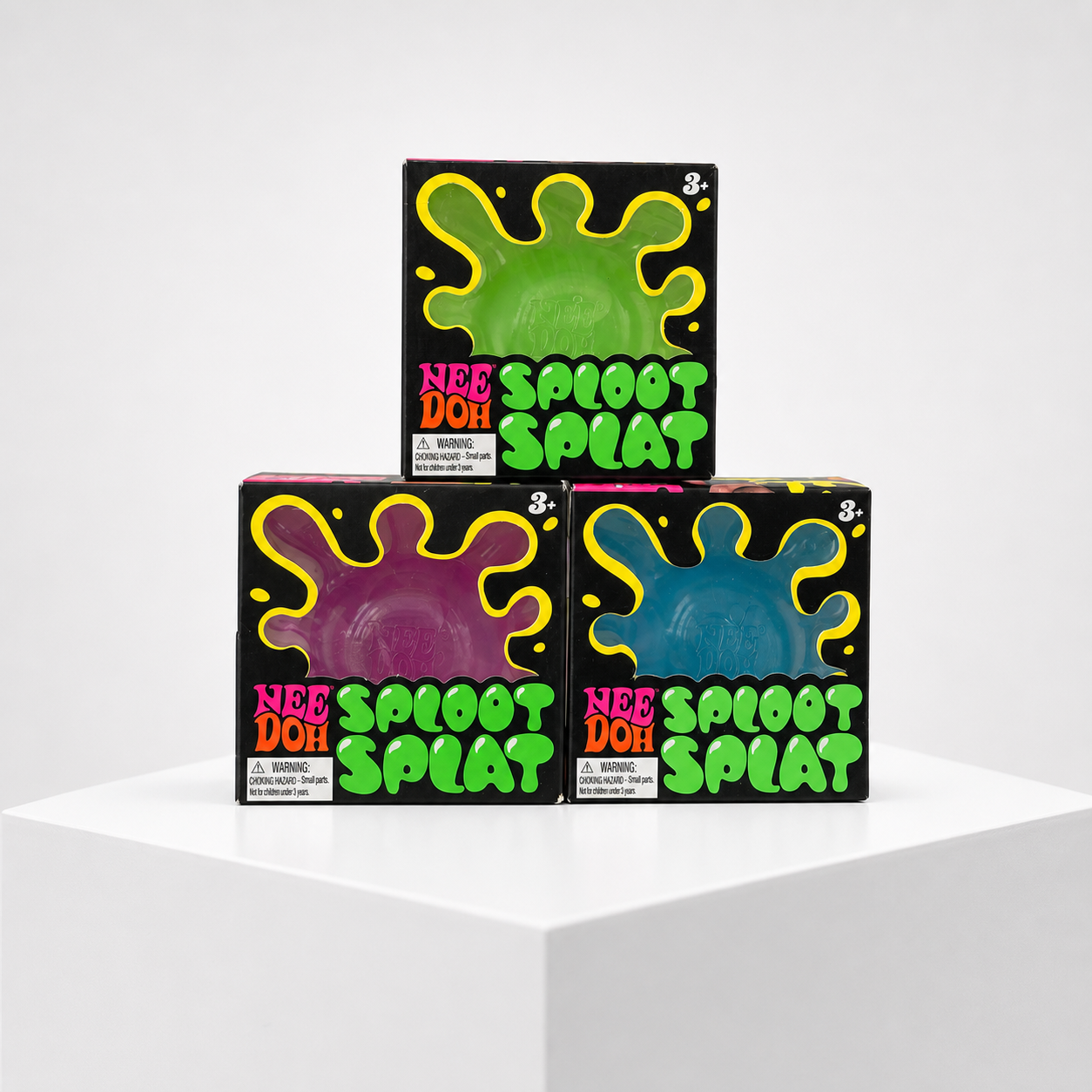 NeeDoh Sploot Splat green, purple, and blue squishy fidget toys in retail packaging on a white studio pedestal.