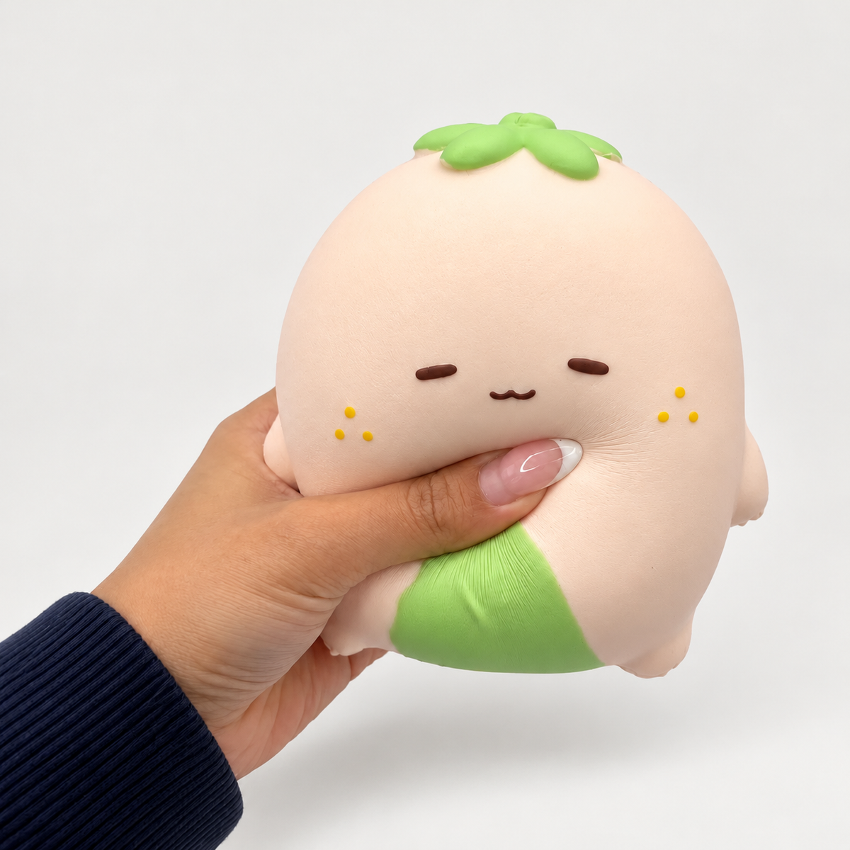 Hand squeezing a pale pink Nunu strawberry character with green details